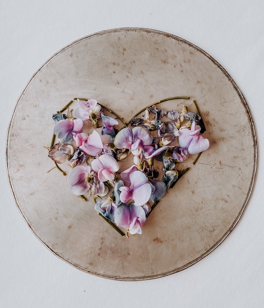 Artistic arrangement of pink and purple petals forming a heart on a vintage round plate, top view.